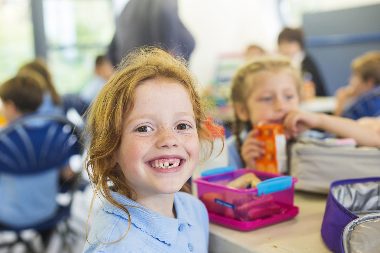 Smiling Girl Missing a Tooth With a Healthy Lunch